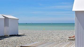 Ein Strand mit einer Holzterrasse, Kieselsteinen und blauem Himmel.