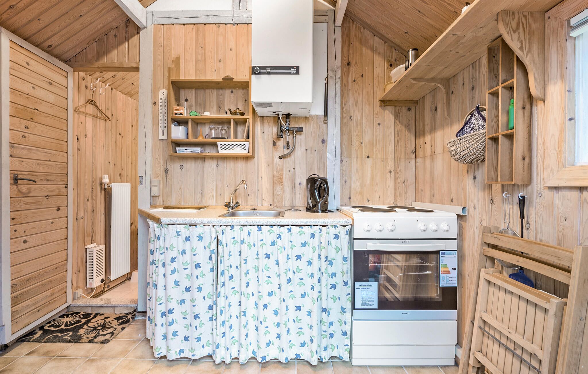 Een kleine keuken met houten wanden, een witte kookplaat, een spoelbak en een hangmandje.