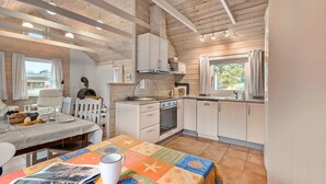 A cozy kitchen with wooden beams, a dining area with a table set for two, and a large window providing natural light. - Amazing home in Skjern with kitchen (Skjern)