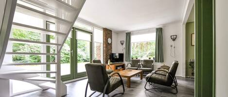 Amplia sala de estar con piso de madera, televisión y chimenea. Hay dos mecedoras y una mesa de comedor.