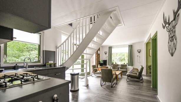 A modern kitchen with a gas stove, a sink, and a window overlooking greenery. A staircase leads to a dining area with a table and chairs.