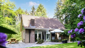 A brick house with a tiled roof, a patio with outdoor furniture, and a garden with trees and flowers.