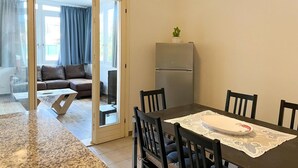 Ein Essbereich mit Tisch, Stühlen, einem Kühlschrank und einer Couch im Hintergrund.