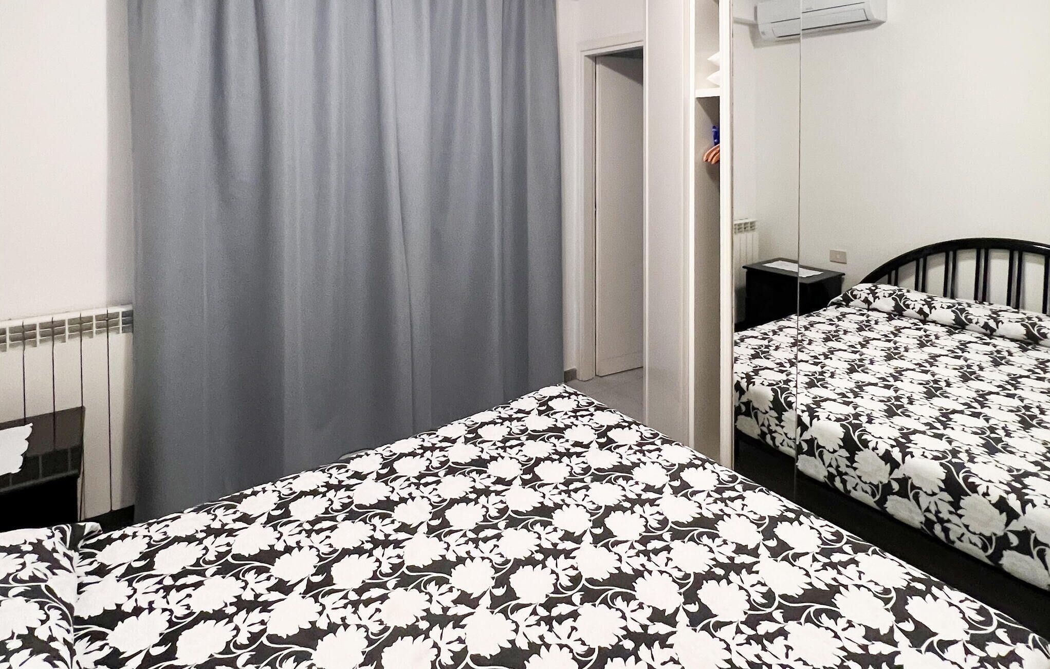 Ein Schlafzimmer mit zwei Betten, einem grauen Vorhang, einem Heizkörper und einem kleinen Nachttisch.