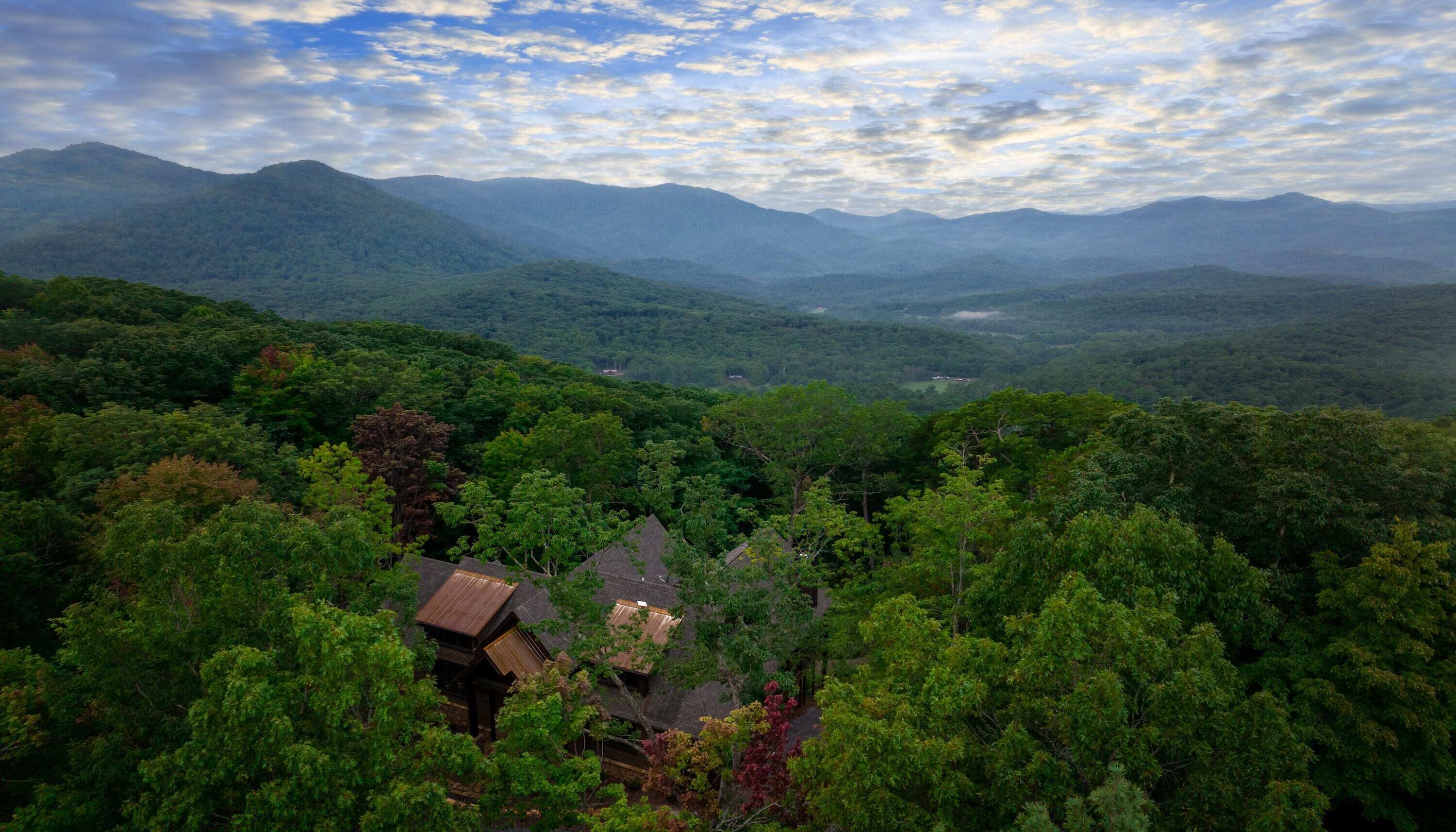 A house surrounded by dense forest with a mountainous backdrop.