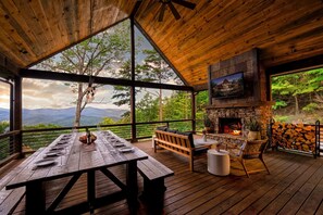 A wooden deck with a stone fireplace, a dining table set for four, and a television mounted on the wall.