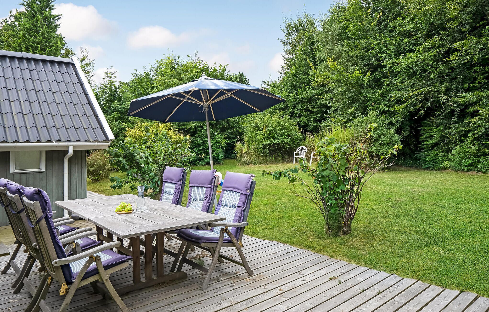 An outdoor deck with a table and chairs, a patio umbrella, and a small shed in a lush garden.
