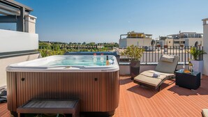 A rooftop terrace with a hot tub, lounge chairs, and potted plants.