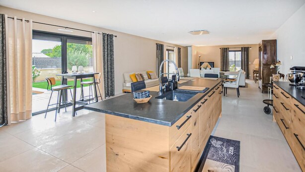 A modern kitchen with a central island, a dining area with a table and chairs, and a living area with a sofa and coffee table. - Beautiful home in Robion (Robion)