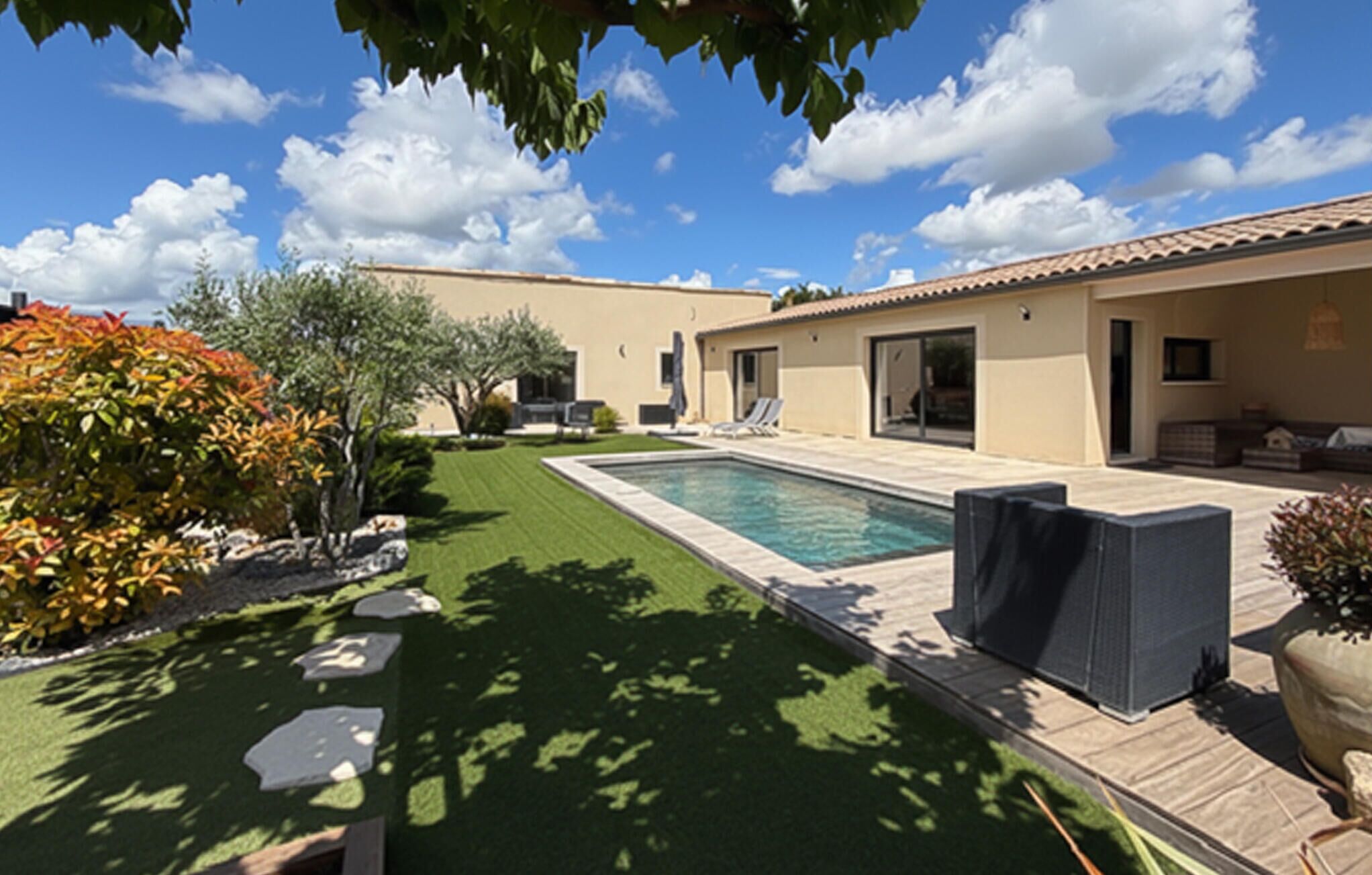 A pool with a patio, a lawn, and a building with a tiled roof.