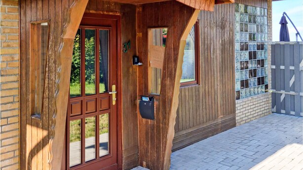 Ein Holzhaus mit einer großen Haustür, einem Briefkasten und einem Fenster mit Blick auf Grünflächen.