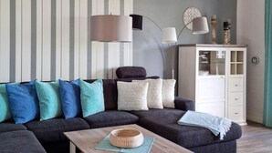 Ein Wohnzimmer mit einem dunkelgrauen Ecksofa, einem Holztisch und einer weißen Vitrine mit Glastüren.