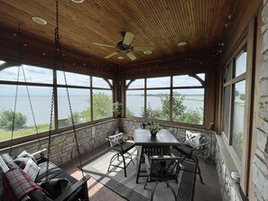 A covered outdoor seating area with a table and chairs, a swing, and a view of the water.