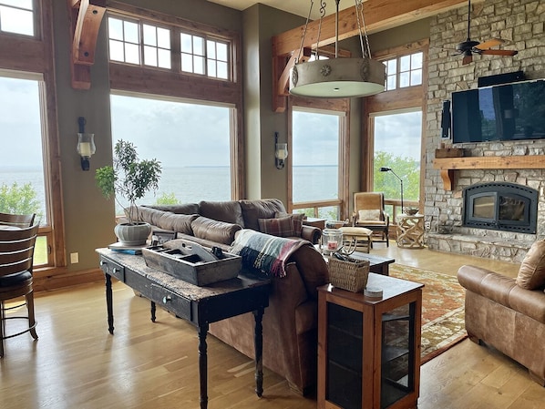 A spacious living room with a stone fireplace, large windows, and a cozy seating area.