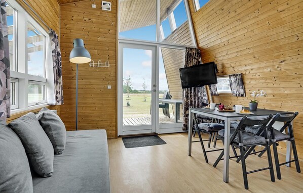 A cozy cabin interior with a sofa, dining table, chairs, a TV, and a large window.