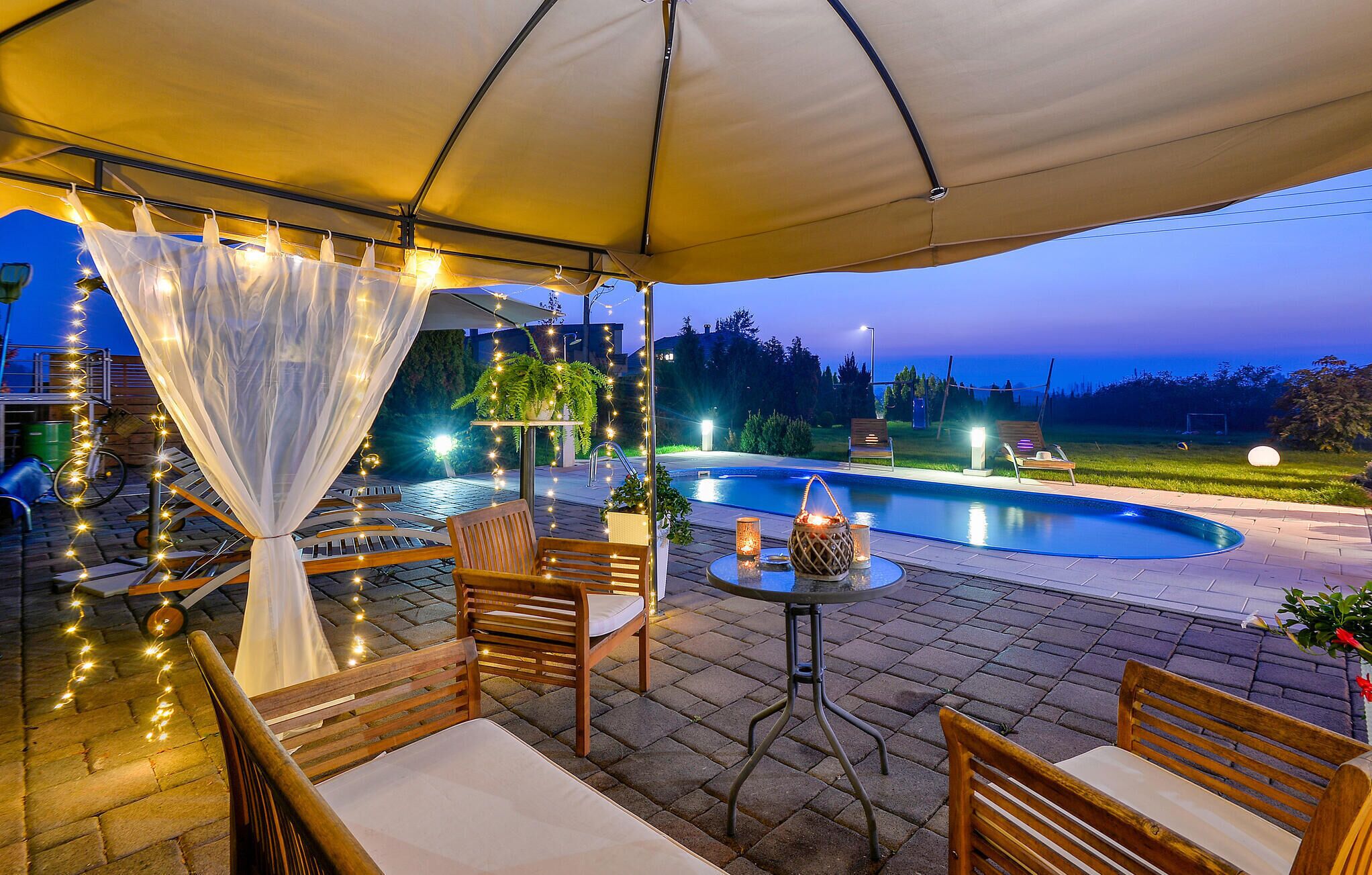 An outdoor patio with a pool, wooden furniture, and string lights.