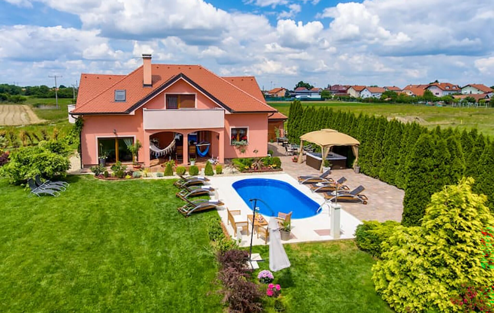 Een huis met twee verdiepingen, een zwembad, tuinmeubilair en een hangmat.