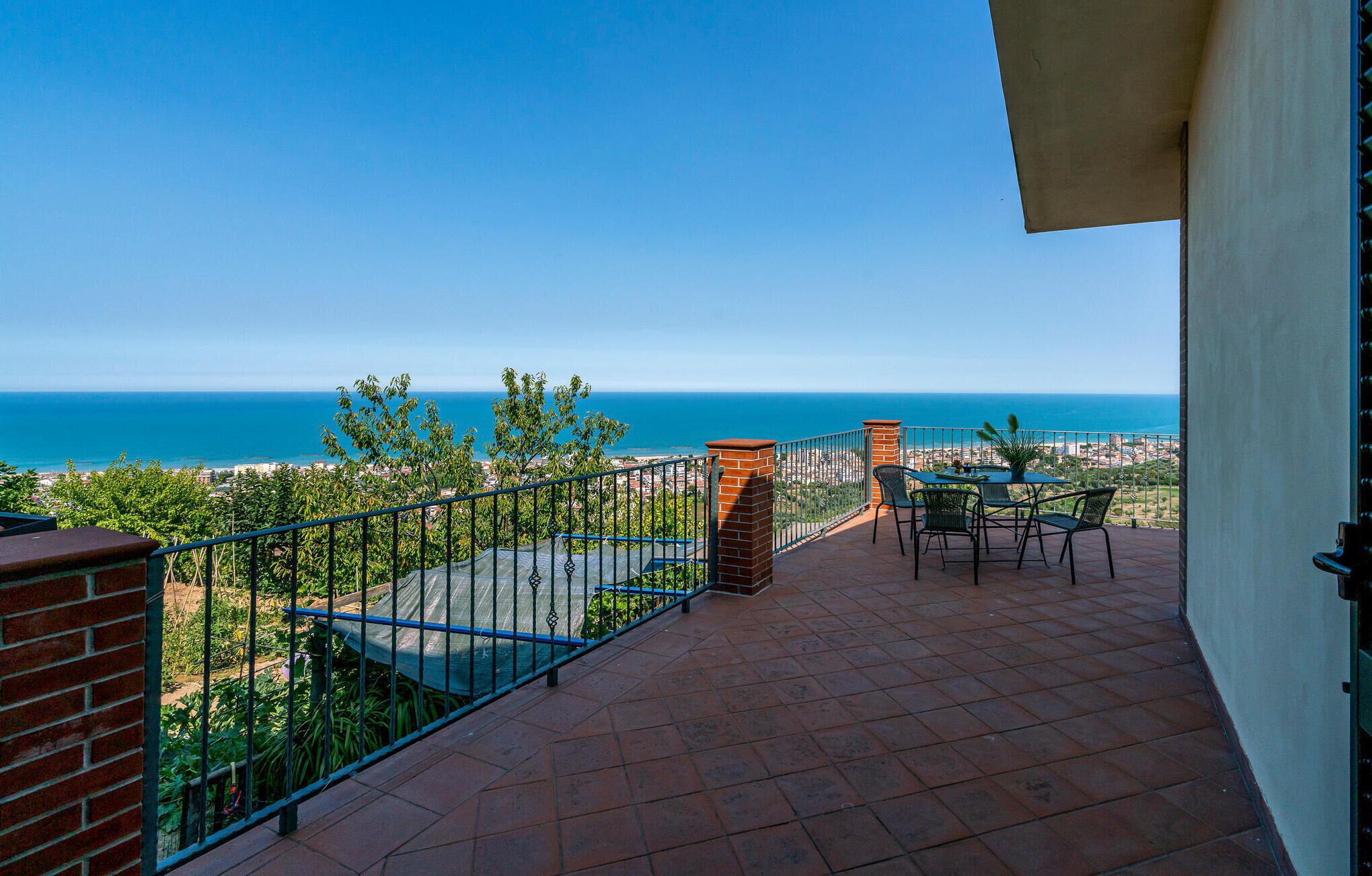Una terraza con vista al mar, una mesa con sillas y una barandilla.