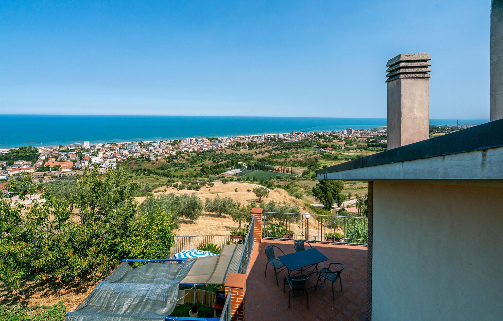Eine Terrasse mit Tisch und Stühlen mit Blick auf eine Küstenstadt und das Meer.