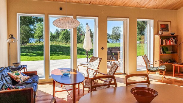 A spacious living area with a large table, comfortable seating, and a view of a lush garden through large sliding doors.