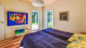 A bedroom with a large bed, a wooden ceiling, and two windows.