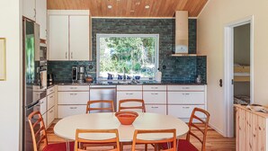 A modern kitchen with white cabinets, a large window, and a dining area with a round table and wooden chairs.