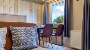 Een gezellige kamer met een bruine bank, gestreepte kussens, een eettafel met stoelen en uitzicht op groen.