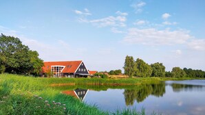 Een traditioneel Nederlands huis met een rood dak, gelegen aan een rustig meer omringd door weelderige begroeiing.