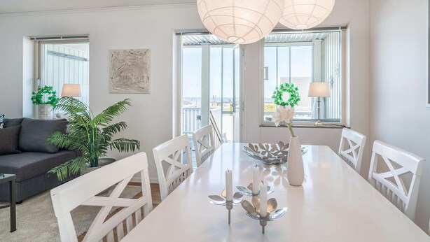 A modern dining area with a white table, white chairs, and a large window offering a view of the sea.