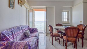 A living room with a purple sofa, wooden dining table, and chairs. There is a balcony with a view of the sea. - 1 bedroom nice apartment in Marina di Caronia (Marina di Caronia)