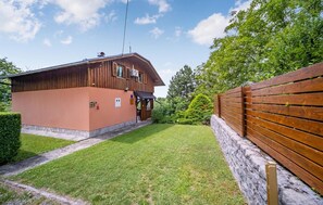 A two-story wooden building with a stone foundation, a wooden fence, and a well-maintained lawn.