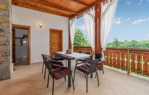 A covered patio with a table and chairs, a wooden door, and a view of greenery.