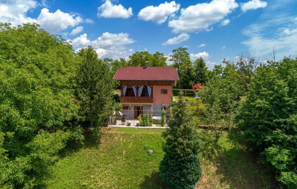 A two-story house with a red roof, surrounded by lush greenery and trees.