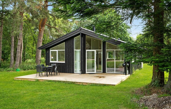 A modern cabin with a deck, large windows, and a black exterior.