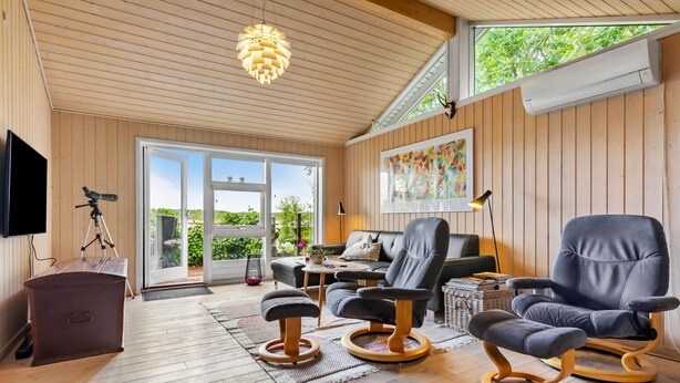 Ett rymligt rum med ett träpanelat tak, ett stort fönster, ett teleskop, en soffa, ett soffbord och en bokhylla.