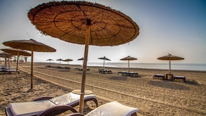 A beach with rows of sun loungers and thatched umbrellas.