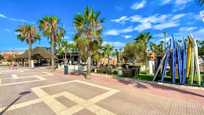 A sunny outdoor area with palm trees, a covered seating area, and surfboards.