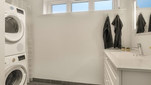 A modern bathroom with a built-in washer and dryer, a large mirror, and a window above the sink.