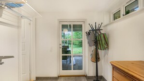 A hallway with a door leading to a patio area, a coat rack with bags, and a wooden dresser.
