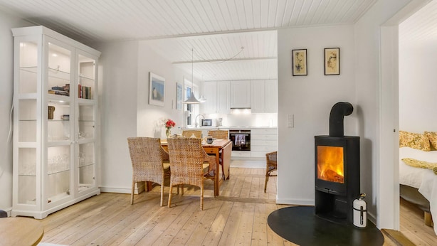 A modern living room with a fireplace, a dining area with wicker chairs, and a kitchen in the background.