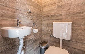 Un baño con pared de madera, un lavabo blanco, un inodoro y un cubo de basura.