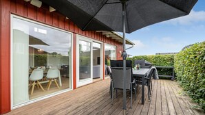 Une terrasse en bois avec une table et des chaises, un barbecue et un grand parasol.