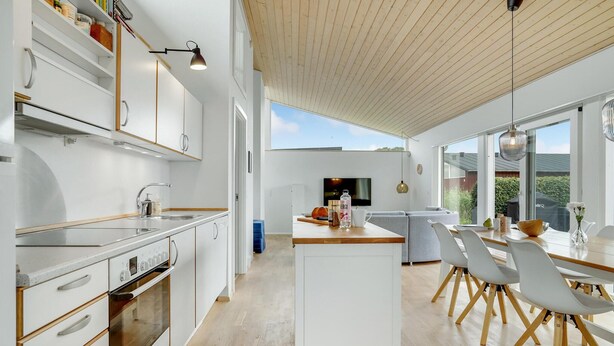 Une cuisine moderne avec des meubles blancs, un îlot central et un coin repas comprenant des chaises blanches et une table en bois.