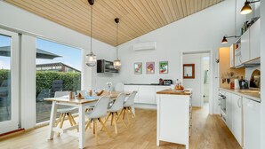 Une cuisine moderne avec des meubles blancs, une table à manger en bois et une vue sur l’extérieur.
