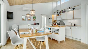 Une cuisine moderne avec des meubles blancs, une table à manger en bois et des luminaires suspendus.