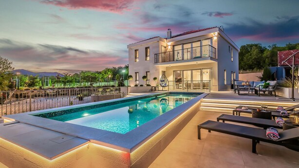 A modern two-story house with a swimming pool, outdoor seating, and a view of the mountains.