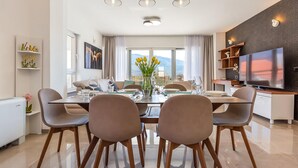 A modern living room with a dining area, a flat-screen TV, and a view of mountains.