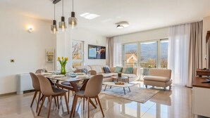 A modern living room with a dining area, large windows, and a view of the outdoors.
