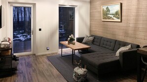 Een gezellige woonkamer met een donkergrijze bank, een houten salontafel en een schilderij aan de muur.