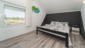 A bedroom with a bed, a nightstand, a lamp, a window with curtains, and a wall decoration. - Beach front apartment in Benkovac with WiFi (Benkovac)